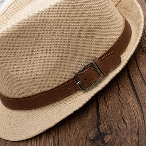 Detail of beige woven straw hat featuring dark brown leather band and silver buckle