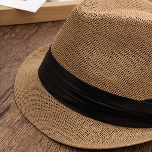 Close-up of natural straw jazz hat with black ribbon detail on a textured wooden desk