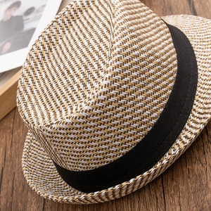 Detail of woven straw fedora hat featuring white and brown fibers with black ribbon band