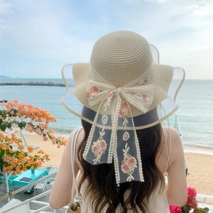 Beige straw sun hat with large pink floral lace bow and wide brim for beach vacation