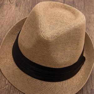 Detailed close-up of woven straw fedora texture with black grosgrain ribbon on wood