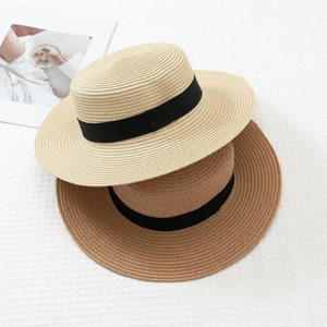 Flat top straw boater hats in beige and camel with black ribbon on textured fabric