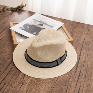 Detail view of woven beige straw fedora with black decorative band on wooden surface