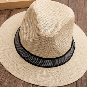 Detailed close-up of beige woven straw fedora hat with decorative ribbon on wood background