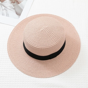 Detail of a pink flat top straw hat with black ribbon on a white textured background
