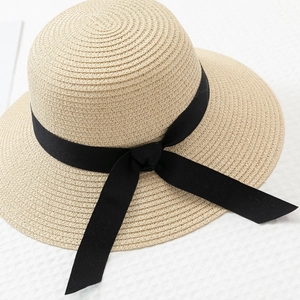 Close-up of straw sun hat featuring a black grosgrain ribbon bow on a beige weave surface