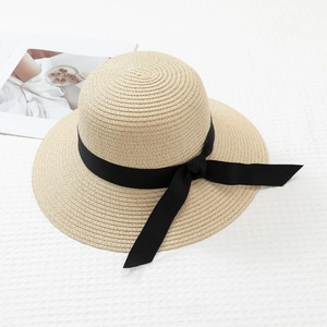 Detail of light beige straw sun hat with elegant black ribbon bow on waffle fabric