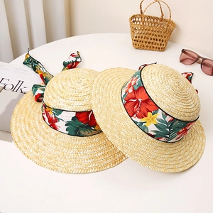 Women's straw beach hats with floral ribbon and bow on a white decorative table