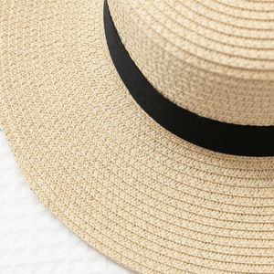 Detailed macro shot of the tight spiral weave and black grosgrain ribbon on the straw hat