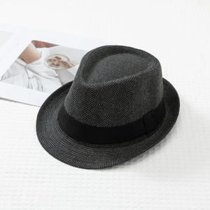 Detailed close-up of dark grey herringbone wool fedora hat on white textured fabric
