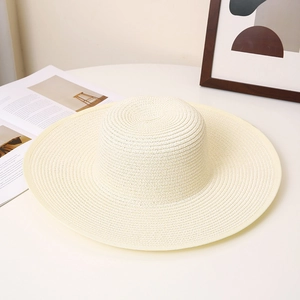 Detail of a wide-brimmed cream straw hat with spiral woven texture on a flat surface