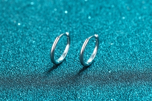 Dettaglio di orecchini a cerchio in argento sterling S925 su uno sfondo glitter blu