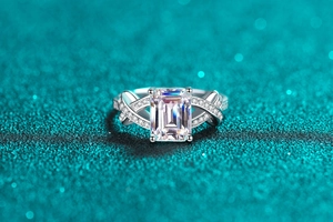 Macro view of emerald cut moissanite ring with a twisted pavé band on a shimmering background
