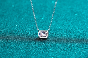 Macro detail of silver S925 necklace with emerald cut moissanite pendant on blue background