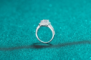 Macro view of S925 silver halo ring featuring emerald cut moissanite on green background