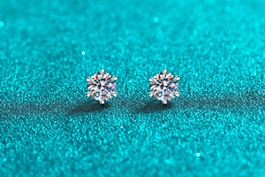 Macro shot of 925 sterling silver six-prong moissanite stud earrings on sparkly teal surface
