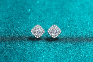 Detail of square-cut moissanite silver stud earrings with diamond halo on green glitter