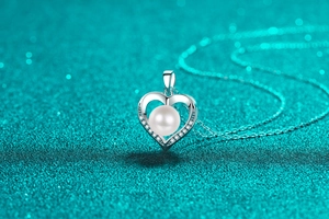 Macro detail of heart-shaped pendant with freshwater pearl on sparkling blue background