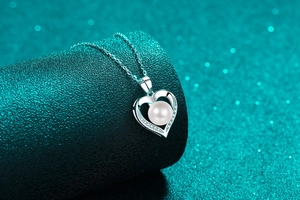 Macro detail of S925 silver heart pendant with freshwater pearl on green display
