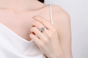 Detailed view of an oval pink moissanite ring with a diamond halo on a model's hand