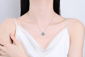 Detail shot of a sparkling heart moissanite pendant on a silver necklace worn by a model