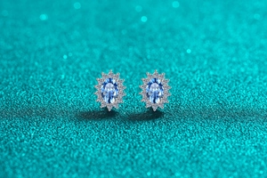 Macro shot of oval blue moissanite stud earrings with white diamond halo on teal glitter