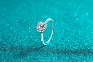 Close-up of a cushion-cut moissanite halo ring with pavé diamonds on a teal background