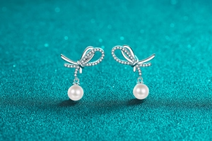 Macro view of silver bow-shaped earrings with moissanite pave and white pearls