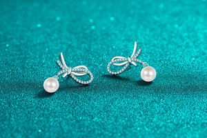 Macro shot of silver bow earrings with moissanite pave and round white pearls