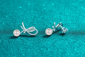 Close-up of S925 silver bow stud earrings with sparkling moissanite and white pearl detail