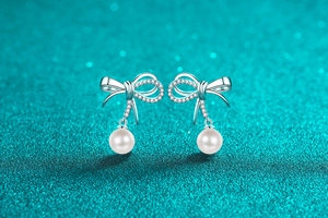 Macro detail of silver bow earrings with sparkling stones and elegant white pearls