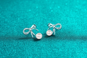Macro detail of S925 silver bow earrings with moissanite and round white pearls