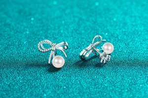 Macro shot of S925 silver bow earrings featuring sparkling moissanite and a round white pearl