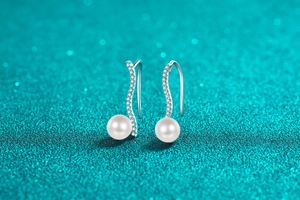 Macro shot of silver wave earrings with moissanite pave and white pearls on blue background