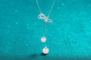 Detail of s925 silver bow pendant necklace with sparkling pavé zircons and pearl tassels