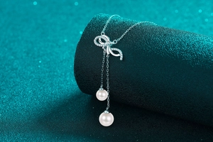 Macro view of 925 silver bow pendant with moissanite pave and twin pearl tassels