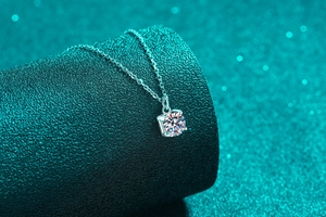 Détail macro du pendentif carré en moissanite sur chaîne en argent S925 et fond sarcelle