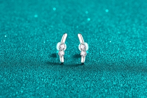 Close-up of S925 silver stud earrings with two sparkling stones on a green glitter backdrop