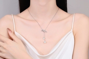 Detail of silver bow pendant necklace with double pearl tassels on a fashion model