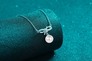 Close-up of S925 silver bow pendant with shimmering moissanite and a round white pearl