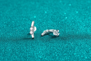 Macro shot of silver rabbit ear moissanite studs on blue glitter background