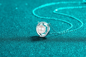 Close-up of S925 silver round pearl pendant with small diamonds on cyan glitter background