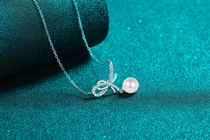 Makroaufnahme von Schleifenanhänger mit Diamanten und runder weißer Perle an Silberkette