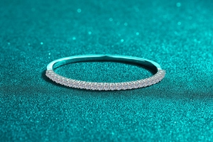 Macro view of S925 sterling silver bangle with pavé moissanite on textured blue background
