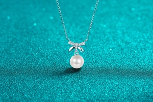 Macro detail of silver bow pendant with sparkling moissanite and round white pearl