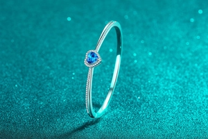 Close-up of heart-shaped blue moissanite gemstone with pavé diamonds on silver bracelet