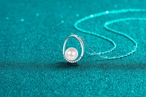 Macro detail of oval pendant with pearl and shimmering stones on a blue background