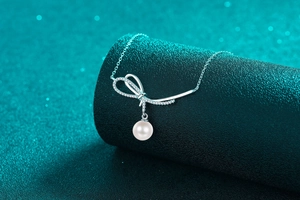 Macro shot of silver bow pendant with sparkling stones and round pearl on a necklace