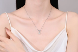 Detail shot of a S925 silver bow pendant necklace with a white pearl on a female model