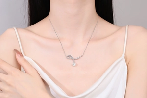 Detail of silver bow pendant necklace with sparkling stones and white pearl on model
